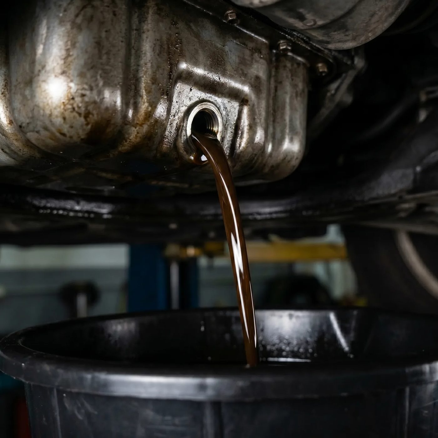 Used engine oil draining into a pan during an oil and filter change